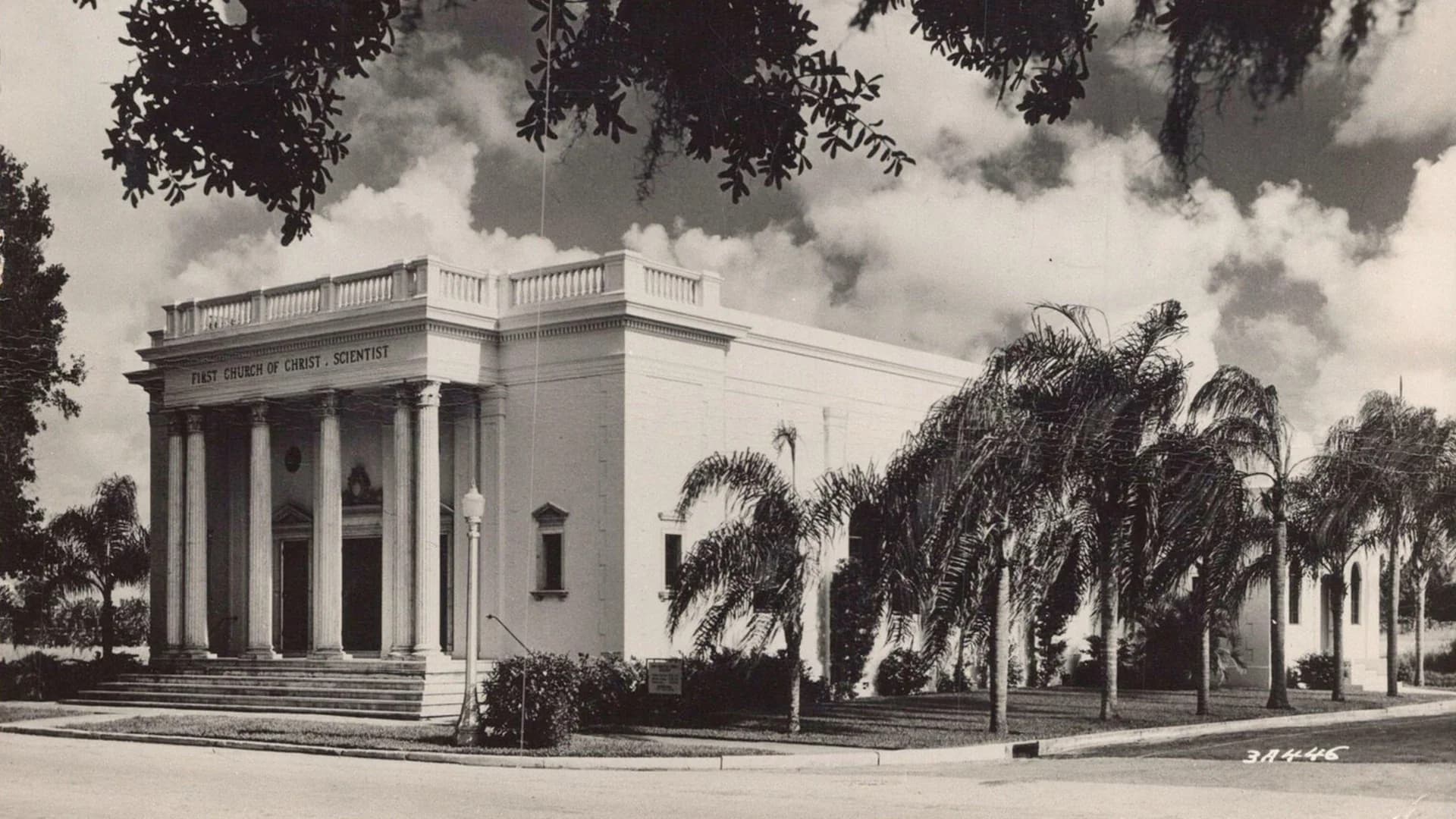 Historic view of the completed church, with a columned entrance and palm trees along the side.